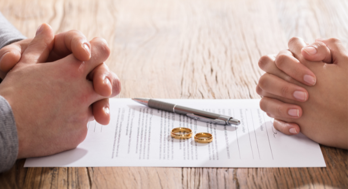 Man and woman's hands folded on table next to divorce decree.