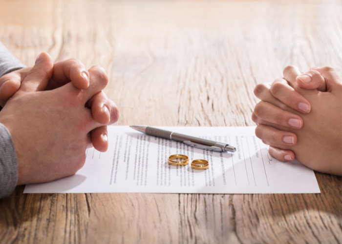 Man and woman's hands folded on table next to divorce decree.