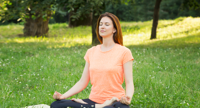 Woman sitting on grass in yoga pose.