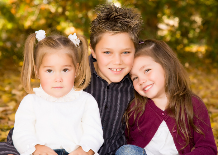 Two little girls sitting with little boy.