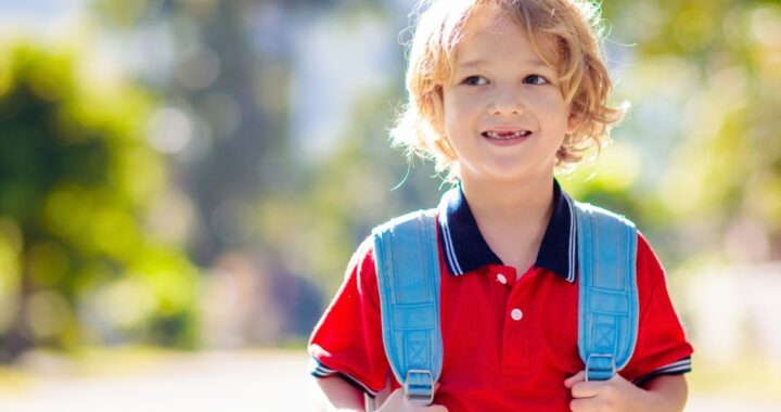 Little boy holding backpack.