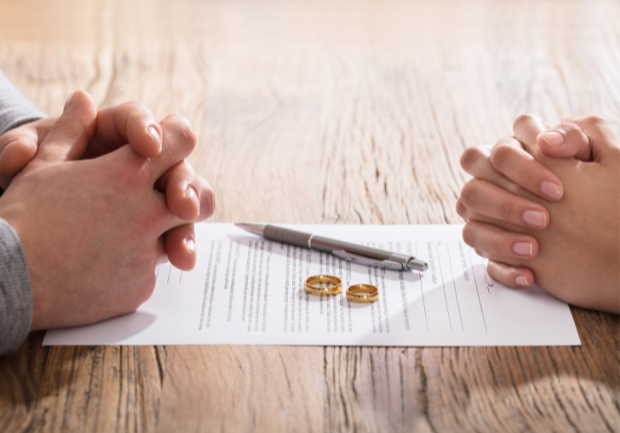 Man and woman's hands folded on table next to divorce decree.