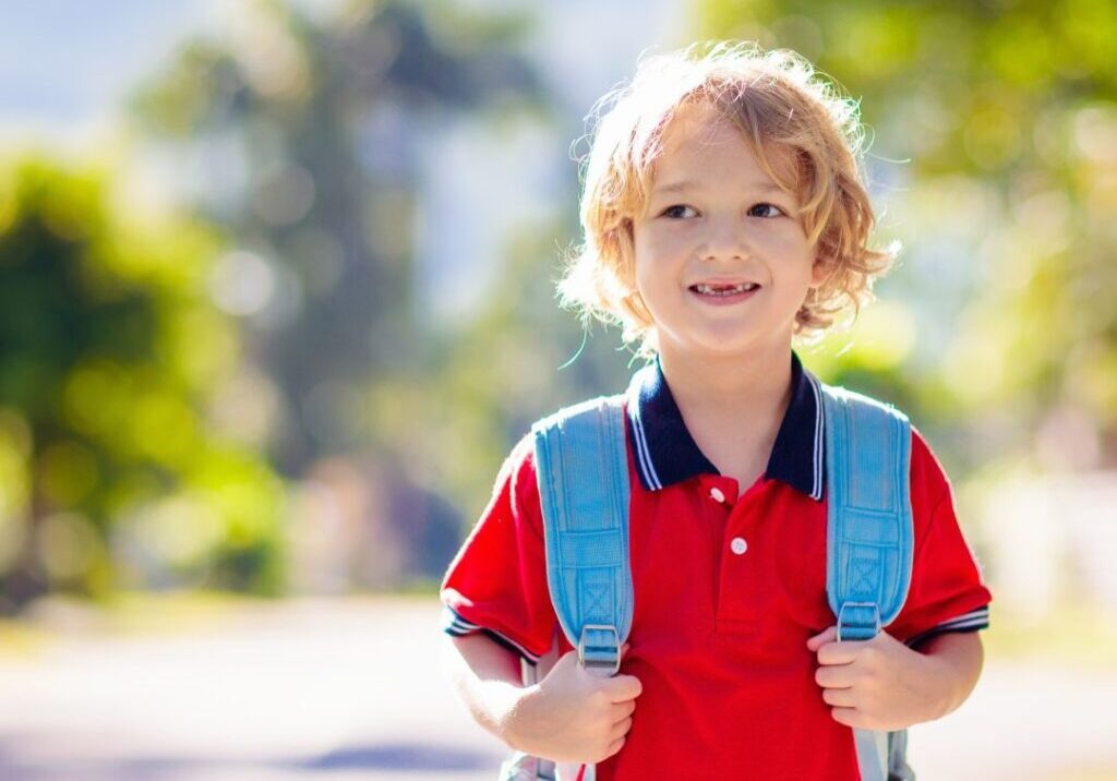 Little boy holding backpack.